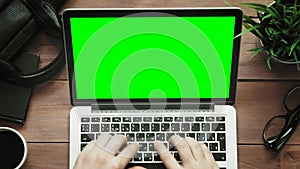 Top view male hands working on laptop computer with green screen at white desk from above