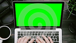 Top view male hands working on laptop computer with green screen at white desk from above