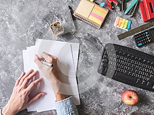 Top view of Male hands writing on paper sheet with Office supplies on Grunge gray background.