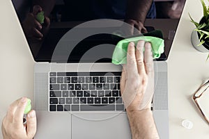 Top view of a male human hands cleaning a laptop screen with cleaning spray and antistatic cloth