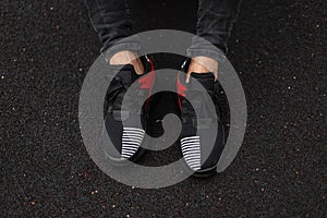 Top view on male legs in trendy sneakers on a black background. Young stylish man in jeans in sports fashionable red-black shoes.