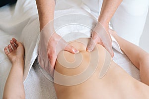 Top view of male masseur massaging lower back of young woman lying on massage table at spa salon.