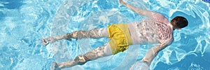 Male person in swimming pants floating on water on belly, clear water in pool