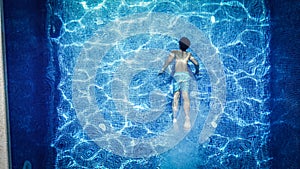 Top view of male in swimwear swimming in transparent pool water with blue tiled floor during summer vacation