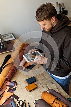 Top view male tanner use tablet at leather workshop. Craftsman creating online advertising promotion photo