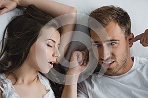 top view of man closing ears and looking at snoring wife