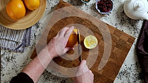 Top view of a man cutting large oranges on a wooden cutting board