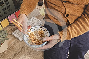 Top view of man eating on working hours, employee holding chopsticks eating takeaway food at workplace in his office