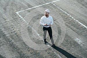 Top view of man in formal clothes and in white hard hat that is walking with tablet in hands