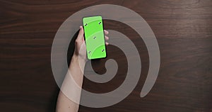 Top view man hand hold smartphone with green screen over black walnut wood table