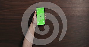 Top view man hand hold smartphone with green screen over black walnut wood table