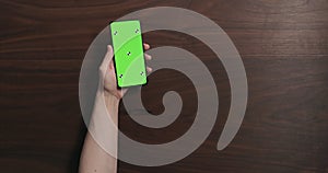 Top view man hand hold smartphone with green screen over black walnut wood table