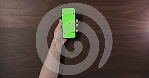 Top view man hand hold smartphone with green screen over black walnut wood table