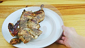 Top view on man by hand moves white plate with half of roasted in herbs chicken