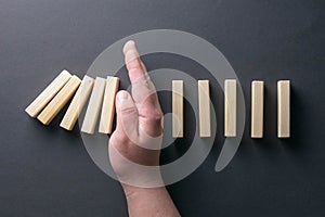 Top view man hand stopping falling dominos in a business crisis management conceptual image