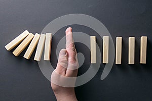 Top view man hand stopping falling dominos in a business crisis management conceptual image