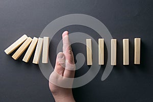 Top view man hand stopping falling dominos in a business crisis management conceptual image