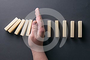 Top view man hand stopping falling dominos in a business crisis management conceptual image