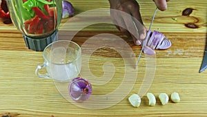 Top view on man hands cut by knife on slices half of purple onion on wooden table