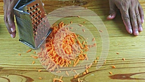 Top view on man by hands grate small slices of fresh carrot on metal grater