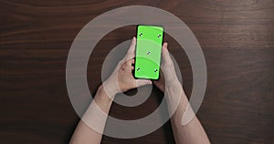 Top view man hands hold smartphone with green screen over black walnut wood table