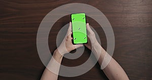 Top view man hands hold smartphone with green screen over black walnut wood table