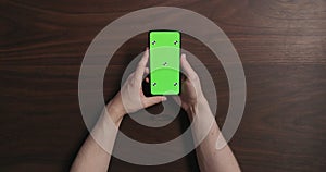 Top view man hands hold smartphone with green screen over black walnut wood table