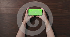 Top view man hands hold smartphone with green screen over black walnut wood table