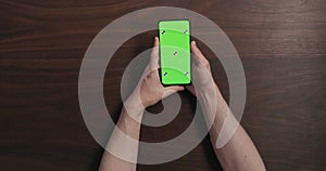 Top view man hands hold smartphone with green screen over black walnut wood table