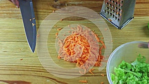 Top view on man hands by knife put grated carrot into vegetable salad in plastic bowl