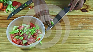 Top view on man hands by knife put green pepper pieces into deep plastic bowl