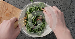 Top view man hands mix salad from radish, cucumbers, kale salad and herbs with dressing