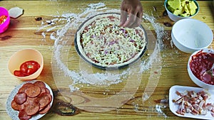 Top view on man hands put onion pieces on semifinished pizza with sauce and cheese