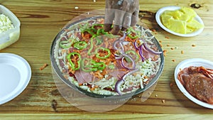 Top view on man by hands put pepper pieces on raw pizza with different ingredients