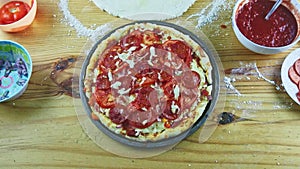 Top view on man hands put pepperoni slices on raw pizza with different ingredients