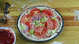 Top view on man by hands put tomatoes slices on raw pizza with different ingredients