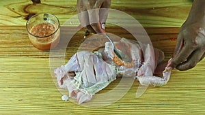 Top view on man hands by spoon marinade half of raw chicken on woodem table