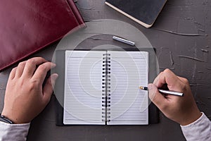 Top view of man hands writing on empty notebook with pen in office.