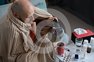 Top view of a man making tea sick at home suffering from high fever and headache. Medicine and healthcare