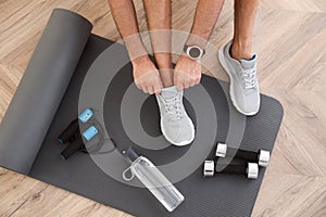 Top view of man putting on sneakers, yoga mat, bottle, skipping rope and dumbbells