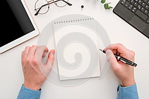 Top view man`s hands with notepad on office desk. Workplace with notebook, tablet, glasses, pen and pin. Flat lay man