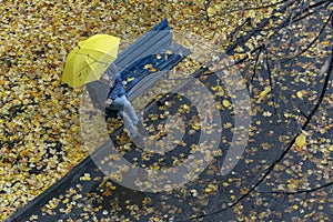 Top view. Man sits on bench in the yard under yellow umbrella, surrounded by fallen leaves