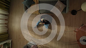 Top view of a man sitting on the living room floor near the couch with a smartphone in his hand. The man is emotional