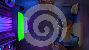 Top view of man sitting on the sofa in the room and losing video game on TV with Chroma key green screen, advertising