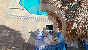 Top View of Man Working on Laptop under Umbrella near Pool in Vacation Hotel