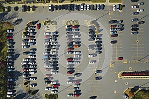 Top view of many cars parked on a parking lot in front of a strip mall plaza. Concept of consumerism and market economy