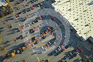 Top view of many cars parked on a parking lot in front of a strip mall plaza. Concept of consumerism and market economy