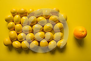 Top view of many ripe lemons on a yellow background next to an orange orange