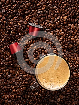 Top view of many roasted coffee beans and glass cup with fresh espresso coffee. Capsules for coffee machines