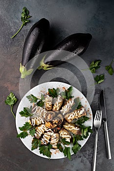 Top view many stuffed eggplant rolls with meat and vegetables on a white plate on grey cement background with cutlery, concept of